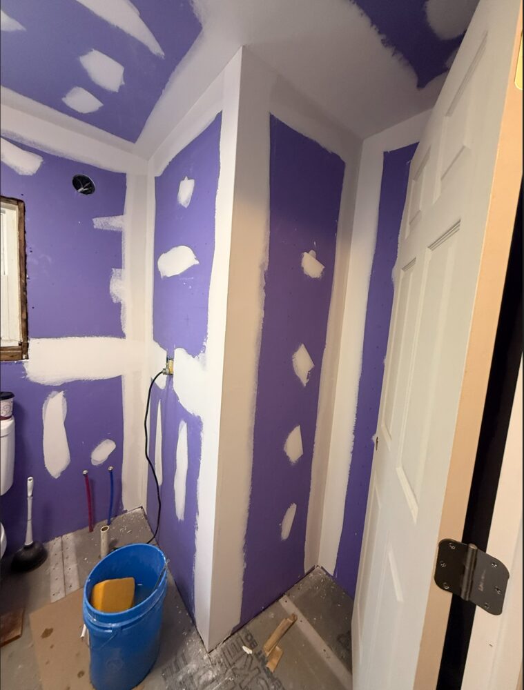 Bathroom before painting: patched drywall with primer and exposed plumbing