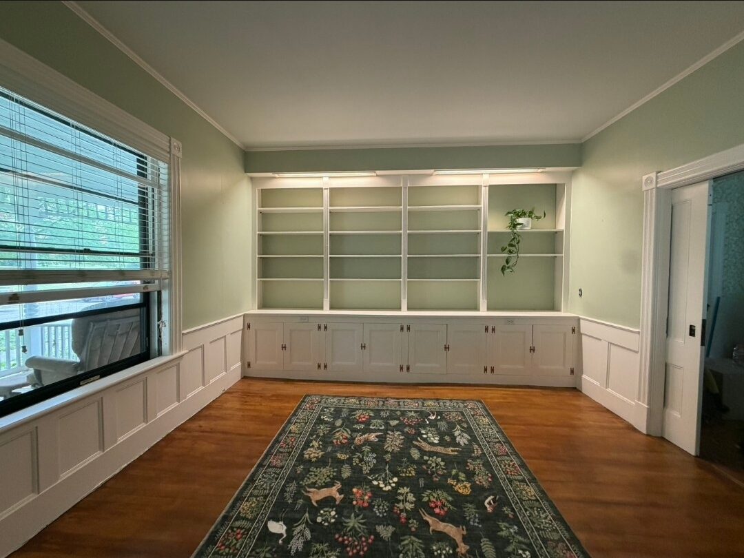 The same sitting room after Eclipse: richly refinished hardwood, soft sage walls and white built-in shelving fitted into the alcoves