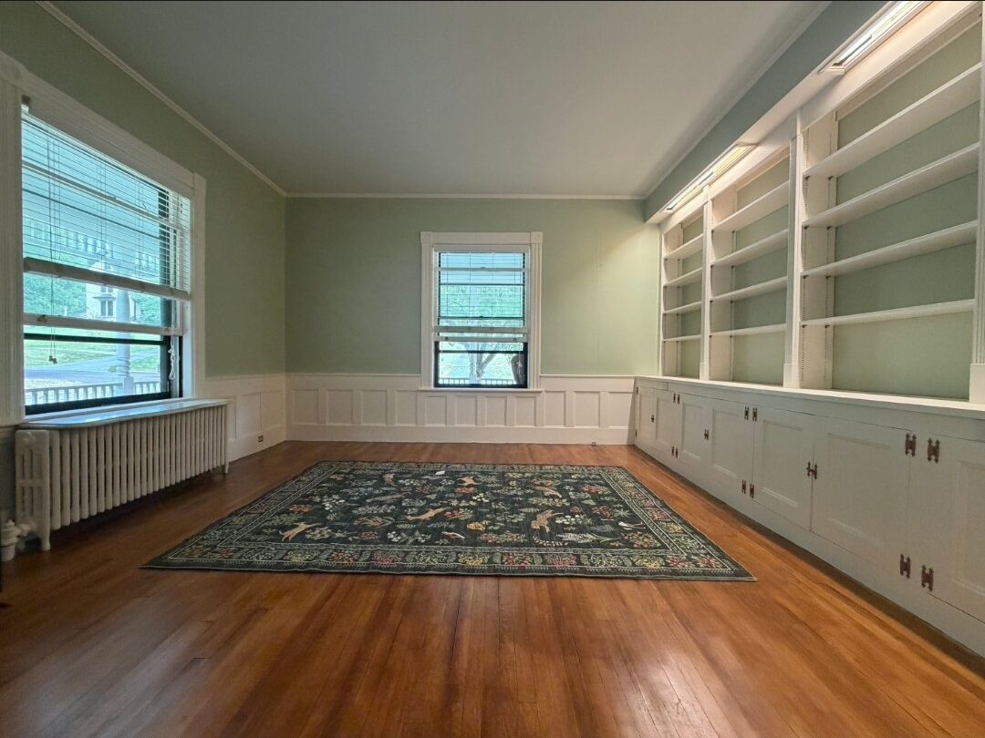 The finished room from that same corner: glossy refinished floors, sage walls, crisp white wainscoting and full-height shelving