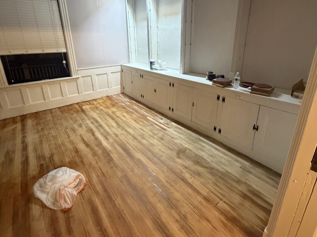 Sitting room before: bare sanded hardwood floor, pale lilac walls and empty built-in alcoves with no shelving